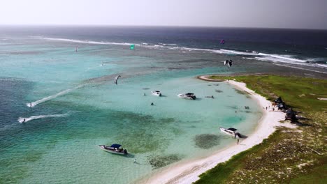 Kitesurfers-enjoy-a-sunny-day-on-a-turquoise-beach-with-boats-and-a-scenic-shoreline-aerial-view