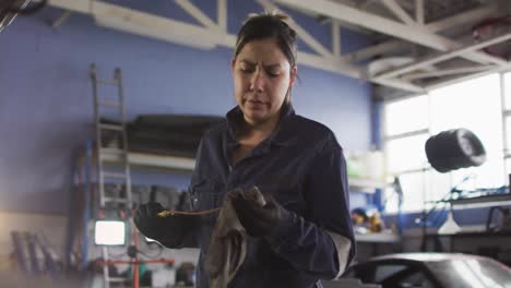 Animation-of-glowing-light-over-biracial-woman-working-in-car-workshop