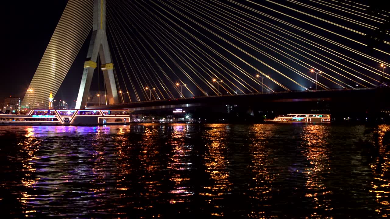 전선 다리 아래의 강에 조명을 은 레크리에이션 보트가 배치되어 있습니다.