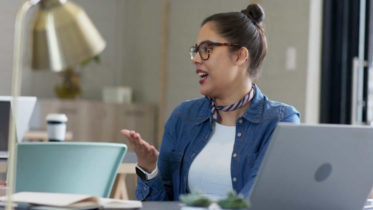 Un collega che parla, una donna che si mette una mano sul cuore, che risponde gesticolando al laptop sul tavolo della riunione