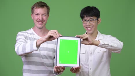 dos jóvenes empresarios multiétnicos felices mostrando la tableta digital a la cámara juntos