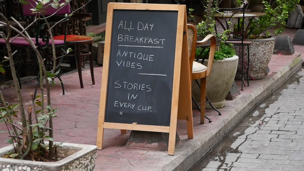 Kridttavleskilt, der reklamerer for morgenmad hele dagen og antikke stemninger uden for en café