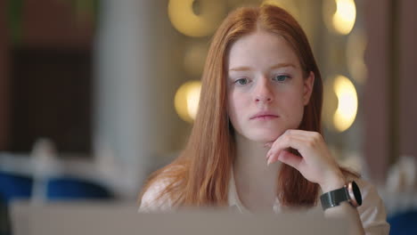 young redhead woman is viewing education video or lecture on display of laptop sitting at home