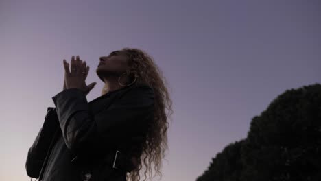 silhouette of a young woman praying alone under the dark sky at night to overcome her depression - close-up shot