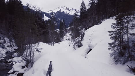 Aerial-view-of-a-small-bridge-over-a-creek-in-a-snowy-valley-in-the-alps,-Kleinwalsertal,Austria