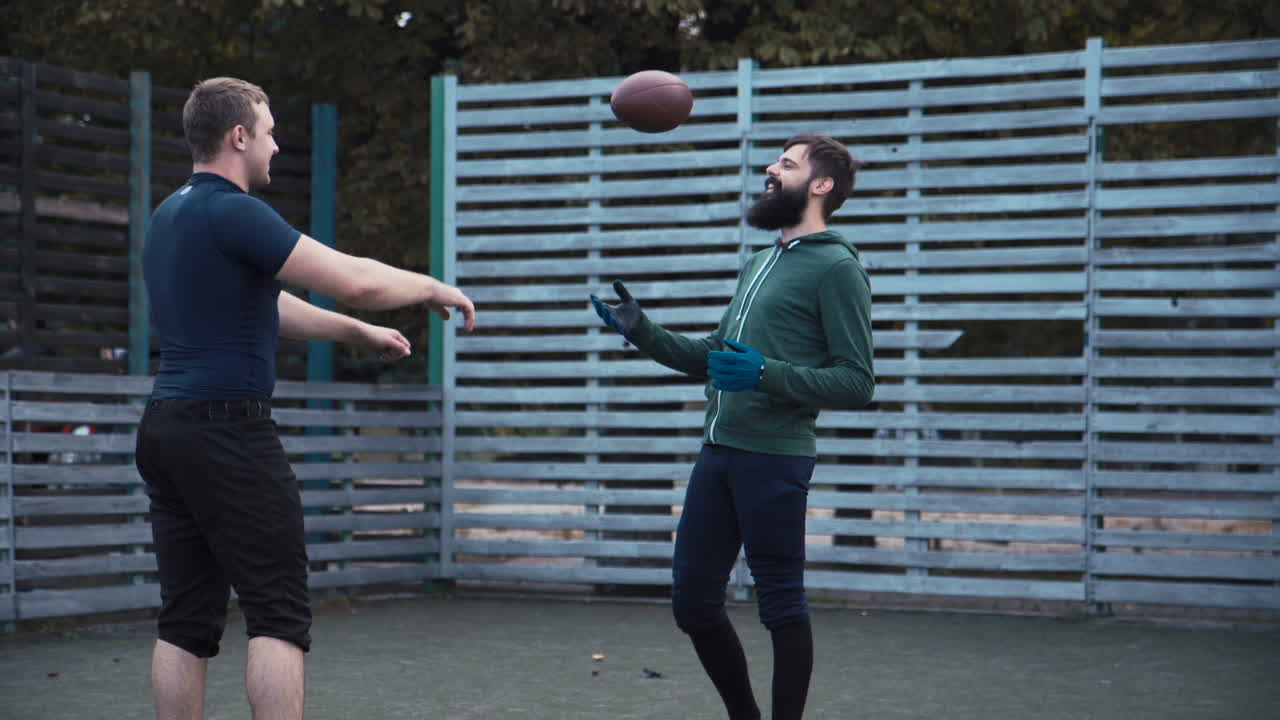 Two men on a field with a football, possibly training or playing
