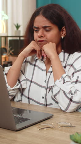 indian woman holding head confused at laptop screen trying struggling with big complex issue indoors