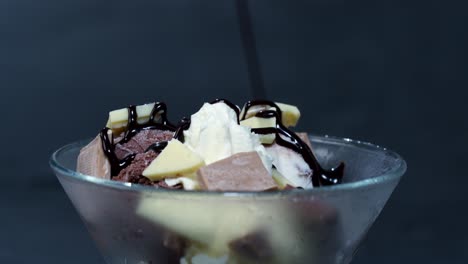 a mug with ice cream balls, cream and chocolate is poured with chocolate sauce