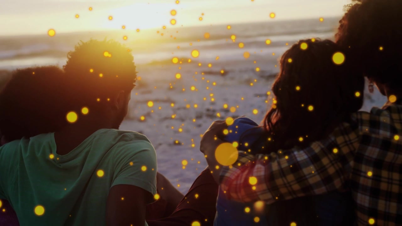 Cuatro amigos sentados en la arena viendo el sol ponerse, con una superposición de partículas amarillas, ajustando un sombrero azul, para marketing