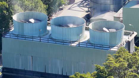 aerial view of large industrial cooling fans on a factory rooftop surrounded by trees.