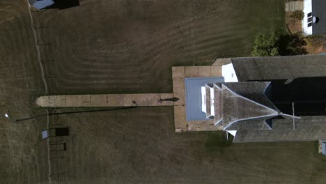 todavía vista aérea de arriba hacia abajo de una persona diminuta que sale de la iglesia y camina por un estrecho camino pavimentado