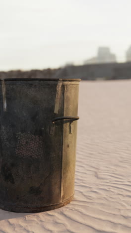 un cubo de metal oxidado en una playa de arena