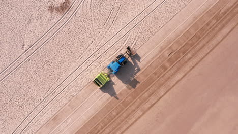 rising tracking shot of a tractor - trailer cleaning a sandy beach in north devon