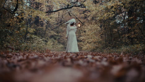 a woman in a white dress holds a glowing lantern in an autumn forest