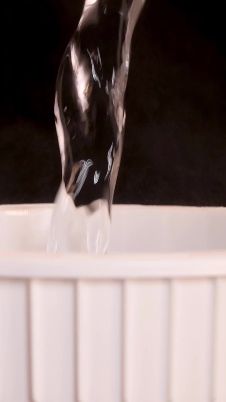 Un flusso costante di acqua calda viene versato in una tazza bianca di noodle istantanei su uno sfondo scuro, catturato in un primo piano con illuminazione morbida e uniforme.