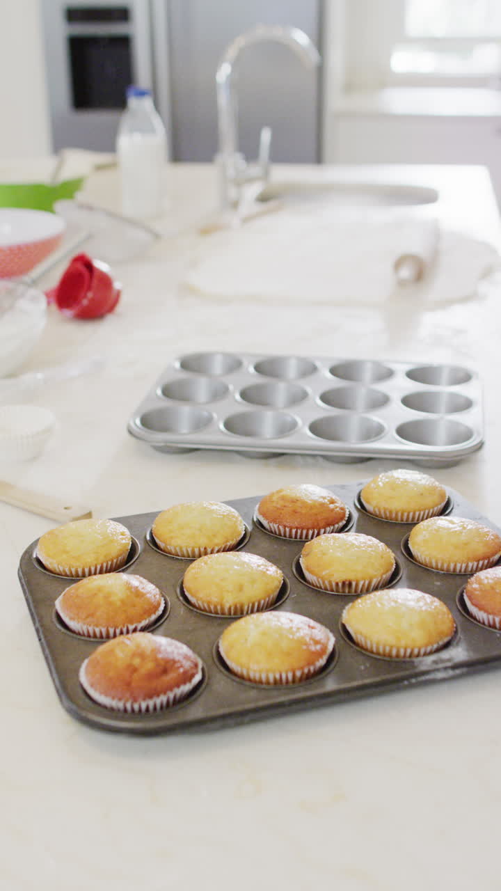 Vertical video of freshly baked fairy cakes in baking tray on kitchen counter, copy space