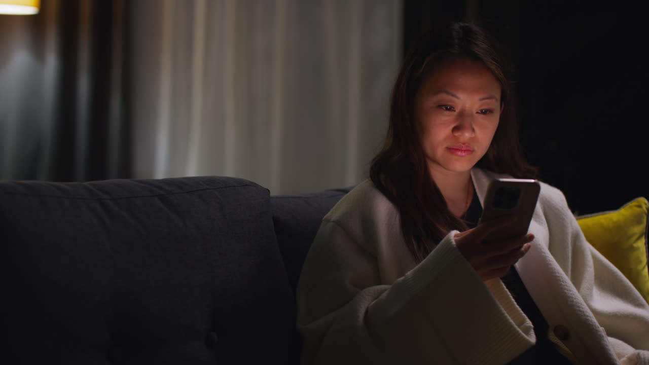 집에서 저녁을 보내고 소파에 앉아 휴대 전화로 인터넷이나 소셜 미디어를 스크롤하는 여성 12