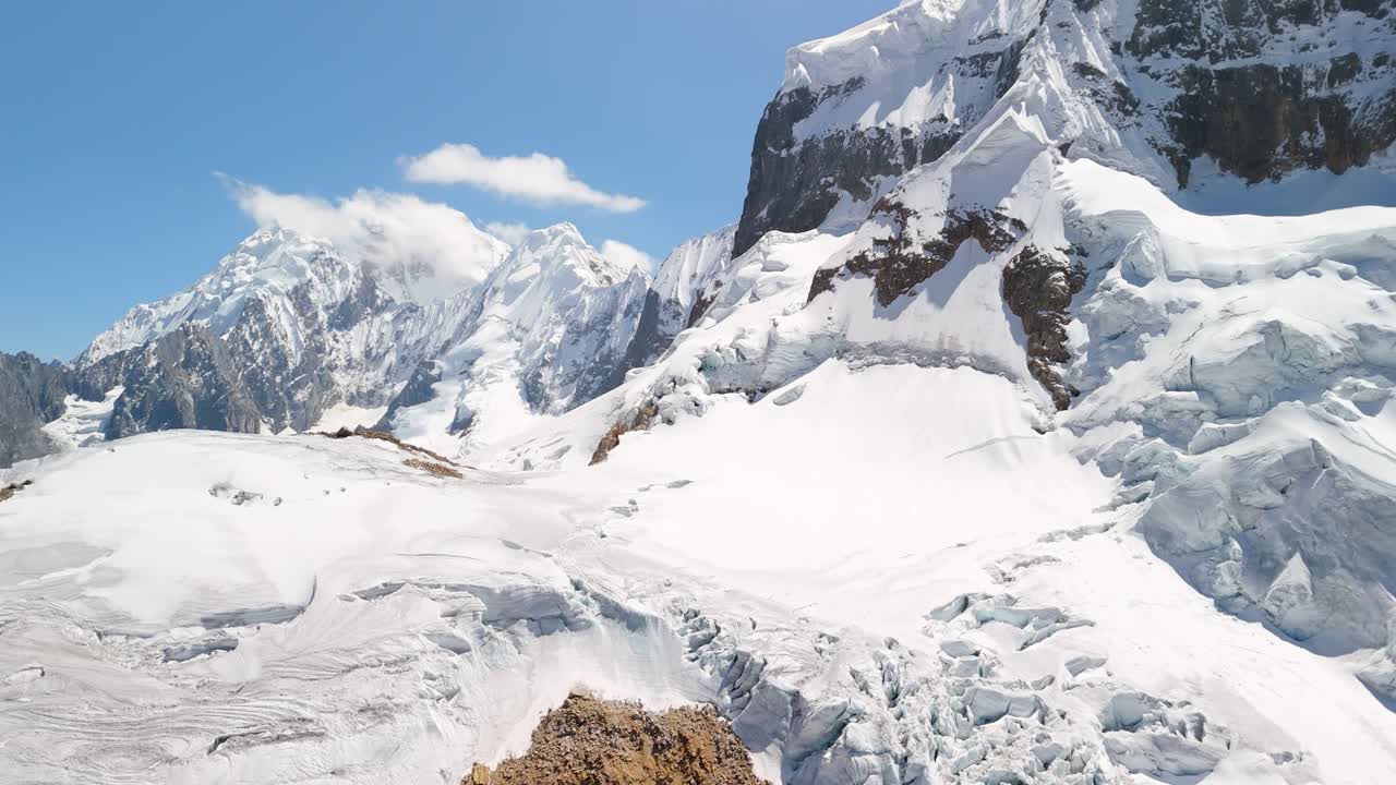 Aerial pan and tilt-up shot reveals the majestic, snow-covered summit of a rugged mountain from the Trapecio Pass on the famous Huayhuash trek in Peru