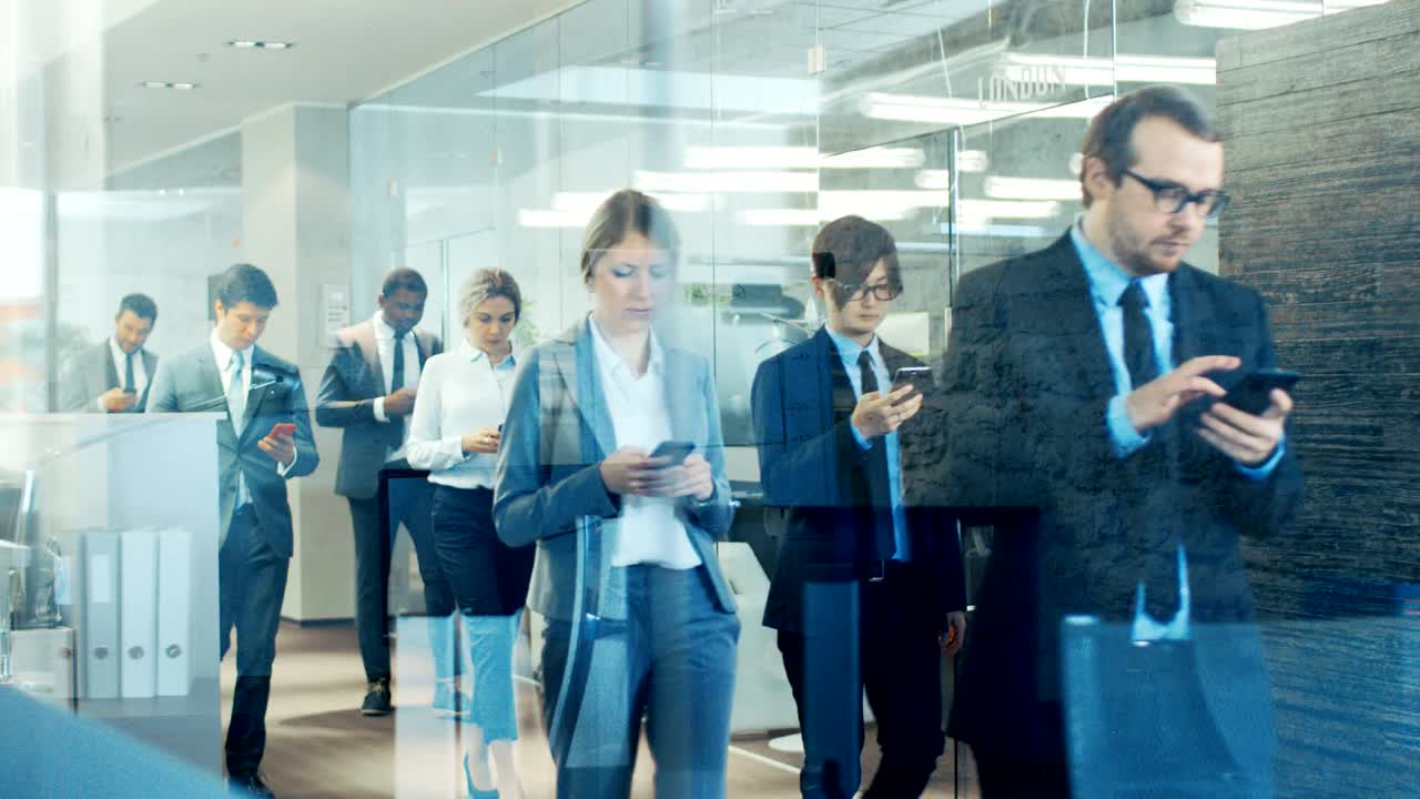 기업 건물 복도를 가로질러 행진하는 사업가들의 유리 장면을 통해 집중된 사업가들의 다문화적 군중이 사무실로 들어오고 있습니다.