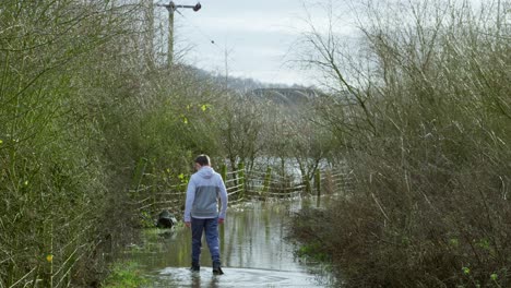 un joven granjero caminando por un camino inundado y atravesando las tierras inundadas.