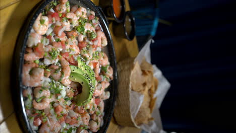 Vertikale-Aufnahme-Eines-Tellers-Mit-Traditionellem-Mexikanischem-Garnelen-Ceviche-Mit-Zwiebeln,-Tomaten-Und-Avocado,-Begleitet-Von-Tortillachips