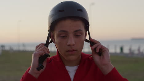 close-up-portrait-confident-teenage-boy-puts-on-helmet-smiling-enjoying-relaxed-summer-vacation-on-seaside-park-at-sunset-slow-motion