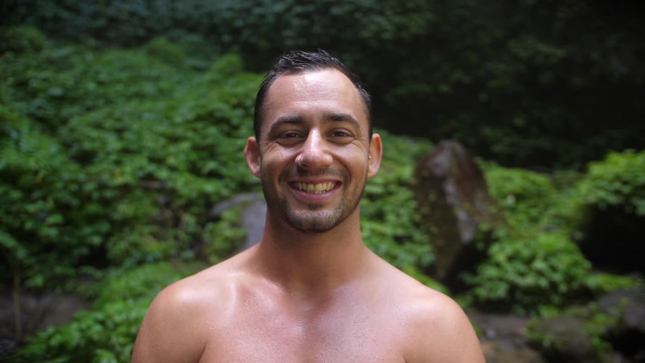 un hombre joven y atractivo con una expresión facial feliz y alegre, mirando a la cámara y a su alrededor en la exuberante y verde jungla de bali mientras sonríe