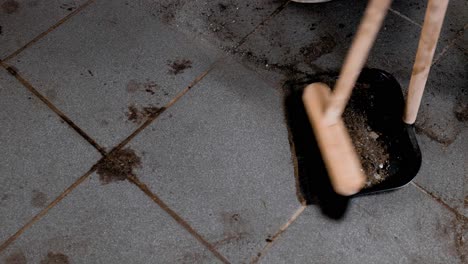 static close up sweeping up dirt in a dust pan from a dirty tiled garage floor.