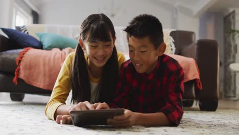 Asian-brother-and-sister-smiling-and-using-tablet-at-home