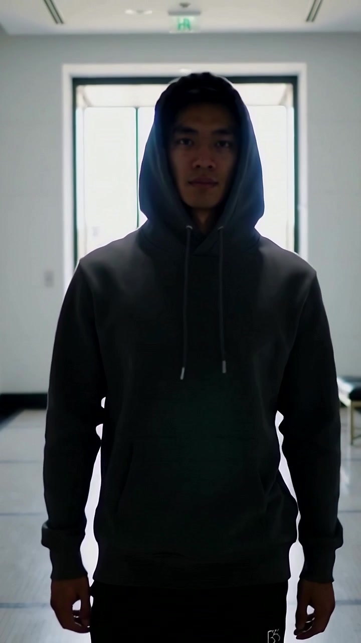 Vertical video: Moving Asian man in hoodie hood up stepping in hallway, reacting to backlit doorway