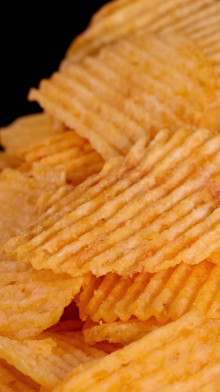 Patatine fritte dorate e ondulate impilate su legno, con zoom indietro e illuminazione drammatica da studio