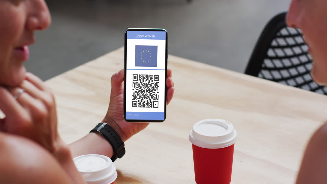 Man at cafe showing smartphone with covid vaccination certificate, eu flag and qr code on screen