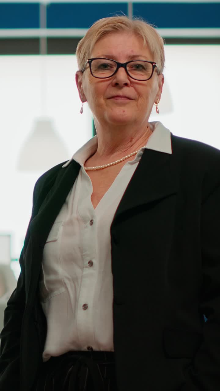 Vertical video Successful senior entrepreneur standing in front of meeting desk looking at camera