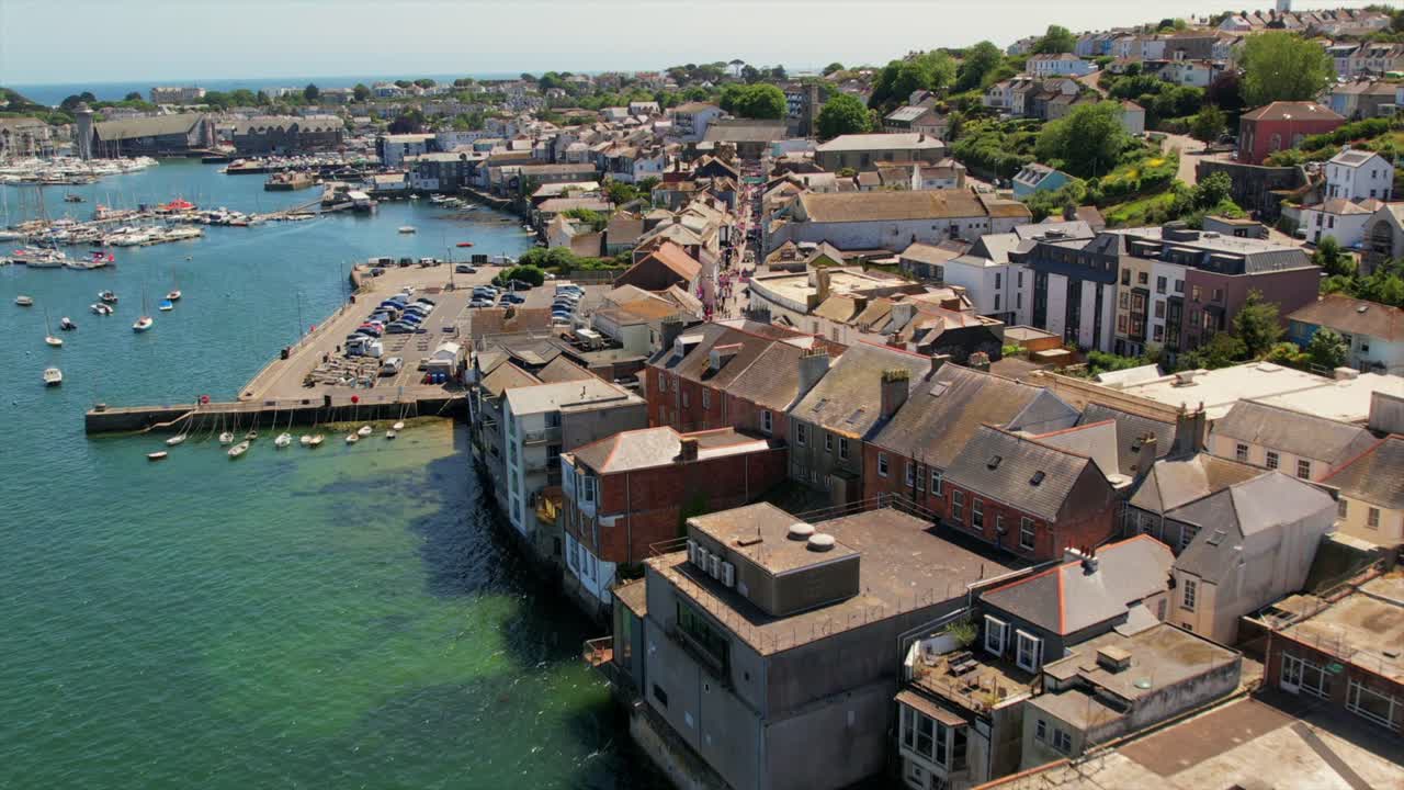 Aerial view of Falmouth harbor showcasing boats, a waterfront promenade, and historic buildings along the coastline on a sunny day.