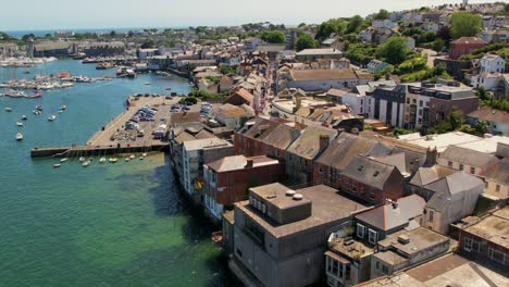 aerial view of falmouth harbor showcasing boats, a waterfront promenade, and historic buildings along the coastline on a sunny day.
