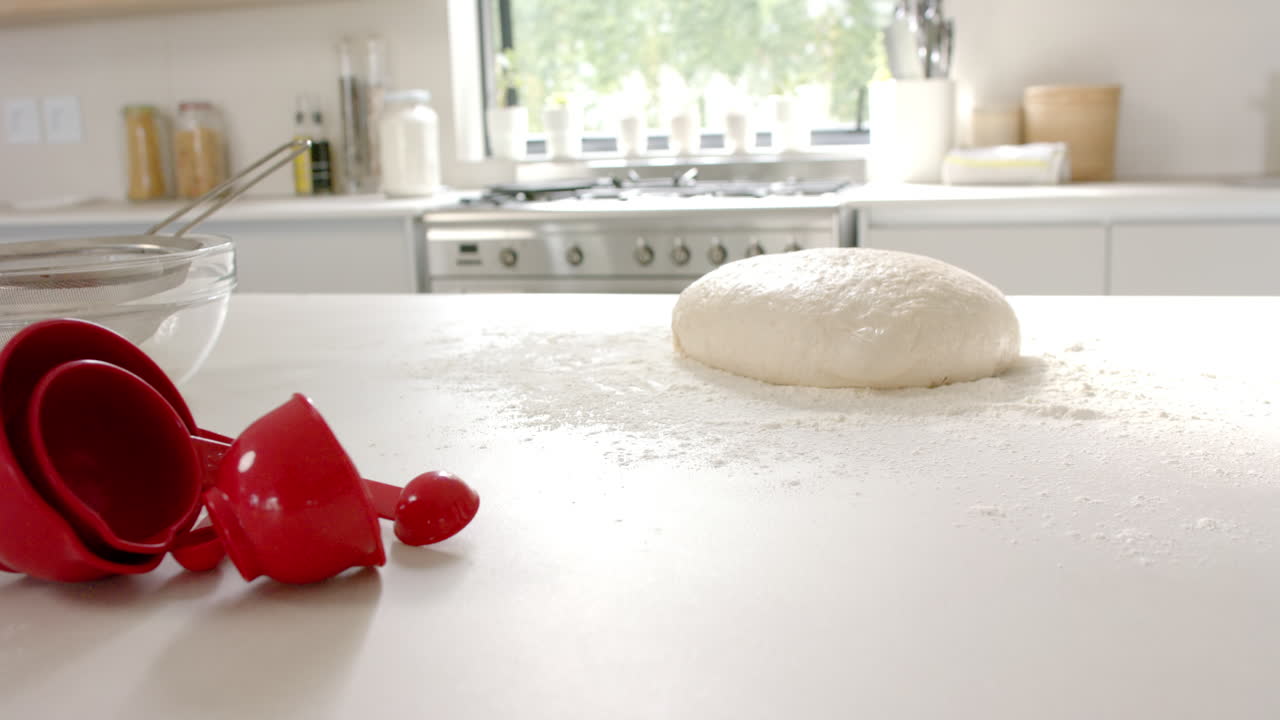 свежее тесто сидит на кухонном столе рядом с измерительными чашками