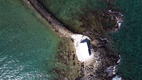 Top-down-view-of-small-white-chapel-surrounded-by-sea