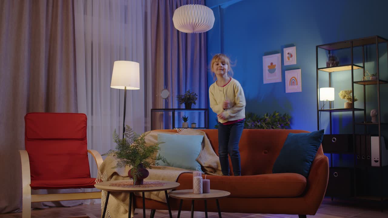 Active funny girl kid jumping dancing fooling on soft cozy sofa at home spend free time alone