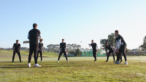 playing cricket outdoors, group of men practicing on grassy field