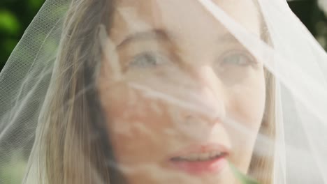 portrait of happy caucasian woman with veil on sunny day at wedding