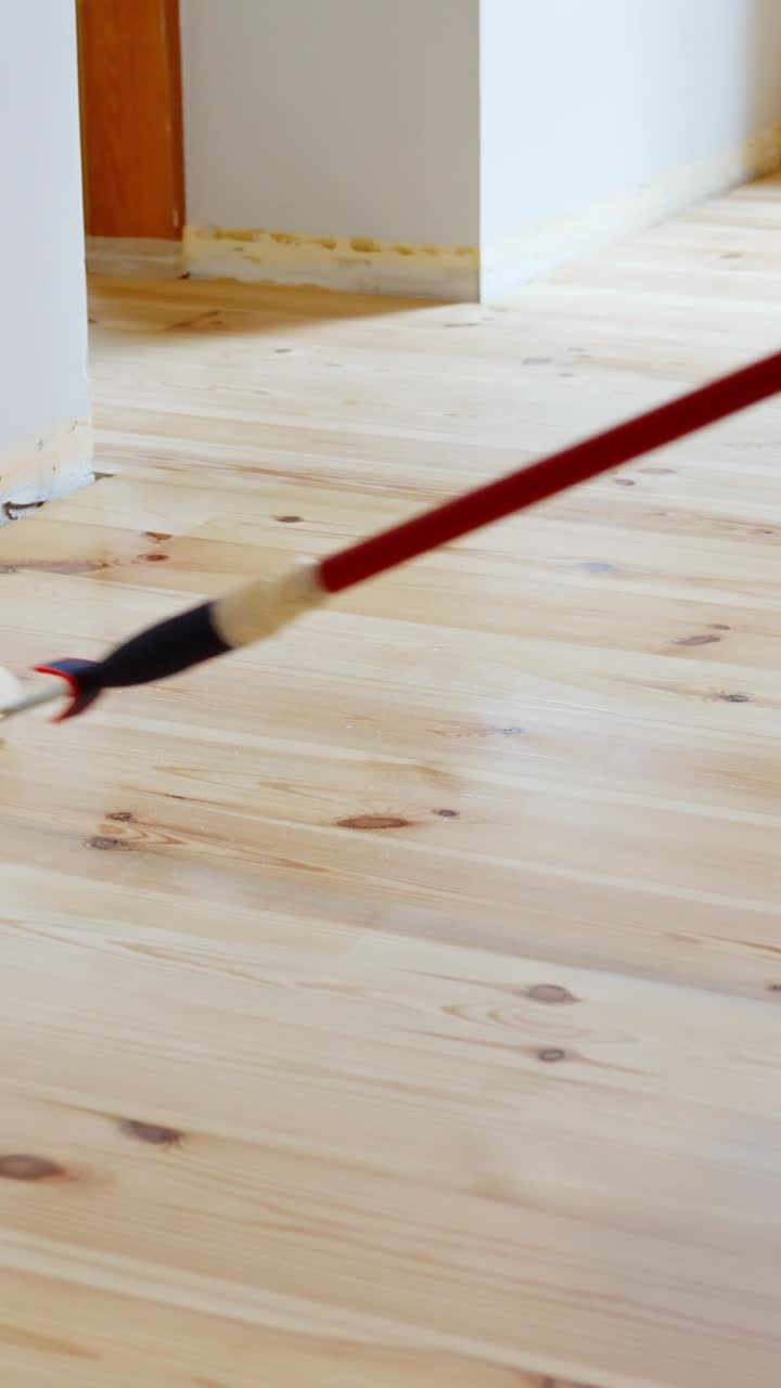Slow motion of roller applying primer on a hardwood floor indoors, vertical