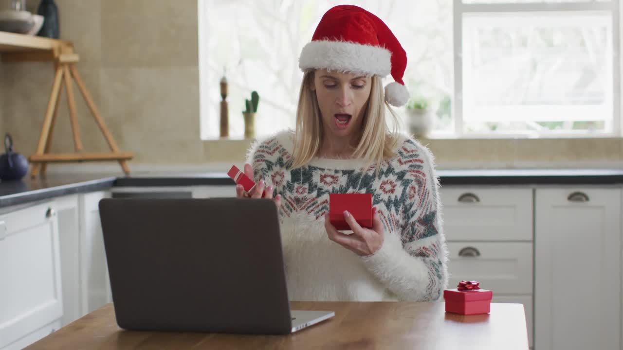 mujer abriendo una caja de regalos mientras hace una videollamada en una computadora portátil