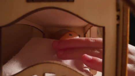 pequeño niño mano toques muñeca acostada en la cama en una casa de juguetes de madera