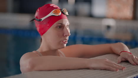 a woman in a red swim cap and goggles stands at the edge of a swimming pool, ready to swim.