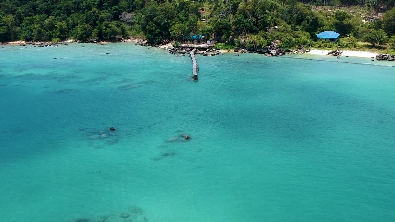 바다 바위와 푸른 바다가 있는 오래된 목조 부두와 녹색 해안선의 공중 기울기 공개