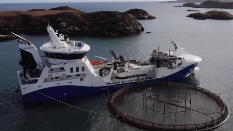 drone shot of a fishing boat docked to a fish farm cage on the hebrides