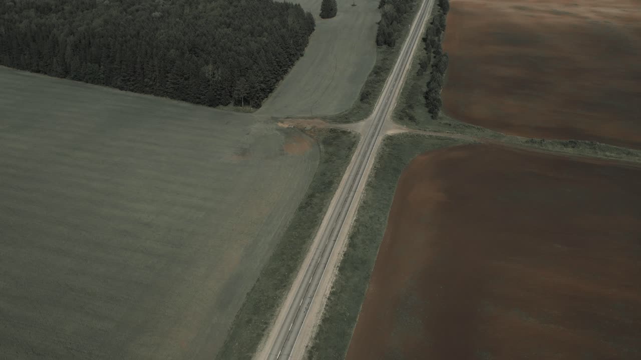 Riprese drone di una strada di campagna dritta che attraversa campi coltivati e il margine della foresta nella regione degli Urali, Russia, mostrando schemi agricoli rurali e la campagna aperta.