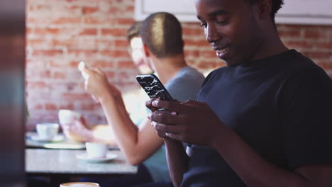 man using mobile phone sitting at table in coffee shop