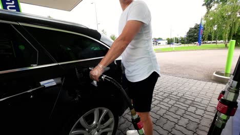 a young caucasian man is filling his luxury black car fuel tank with gas in the station