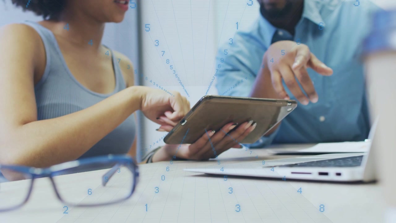 Femme tapant sur une tablette et pointant vers un ordinateur portable, homme penché et pointant, examinant des dossiers professionnels
